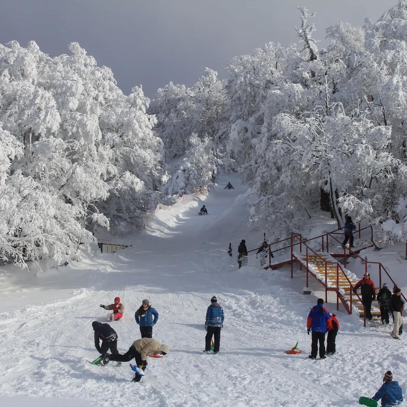 A group of people enjoy a large snowy patio as more people on sleds complete their ride