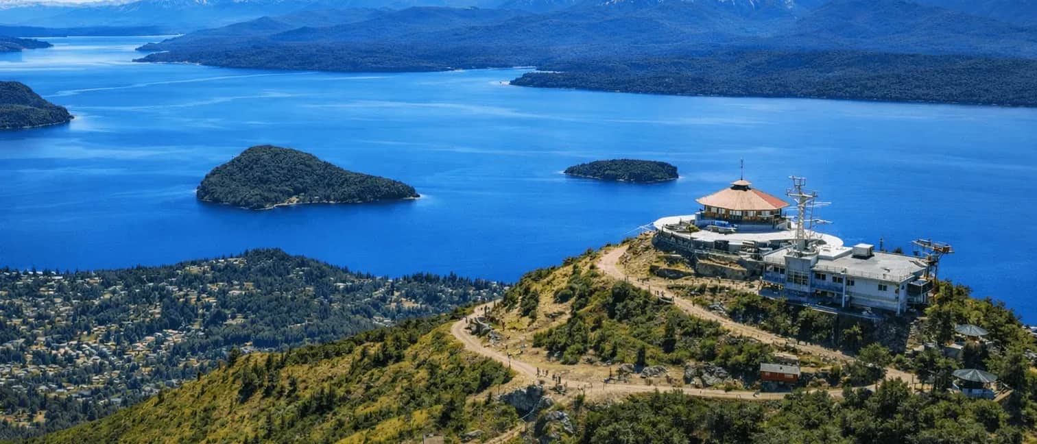 Vista panorâmica do topo do Cerro Otto com a confeitaria giratória e o Lago Nahuel Huapi rodeado por montanhas e florestas, Bariloche.