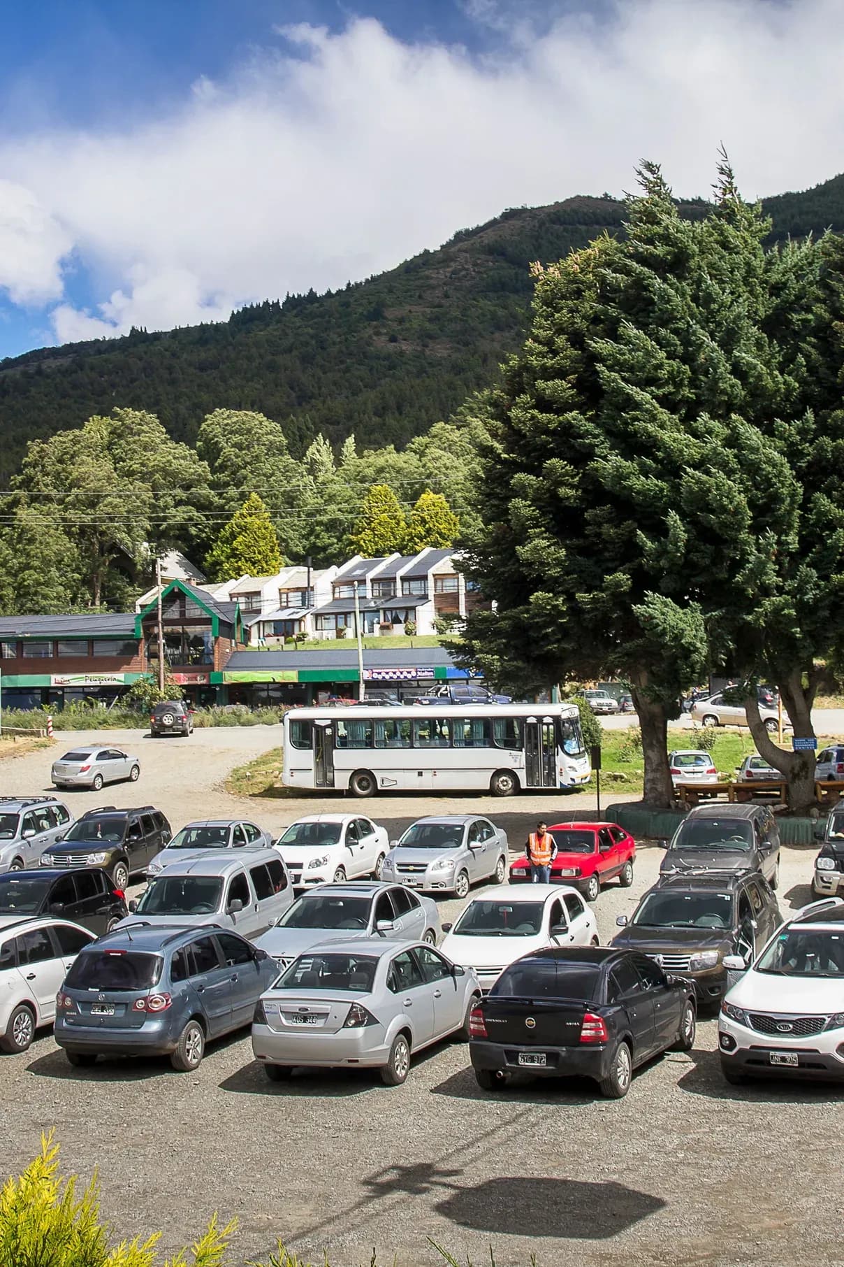 Estacionamento na base do Teleférico Cerro Otto, com um teleférico subindo e carros abaixo.