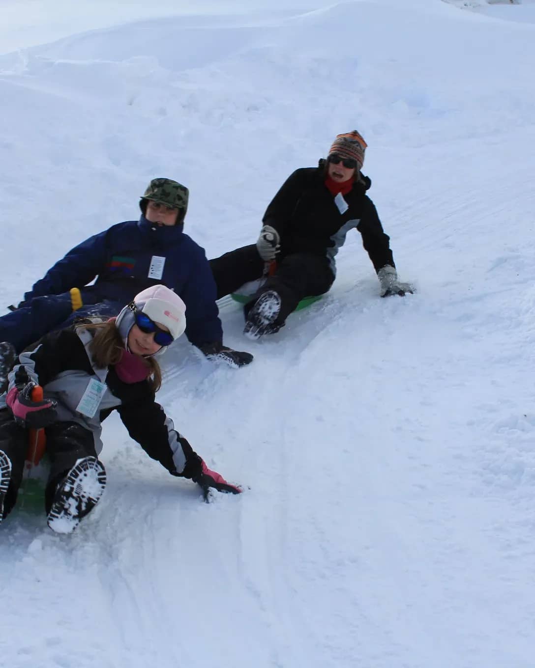 Three people in a row turning around a banked curve while descending the toboggan run at high speed