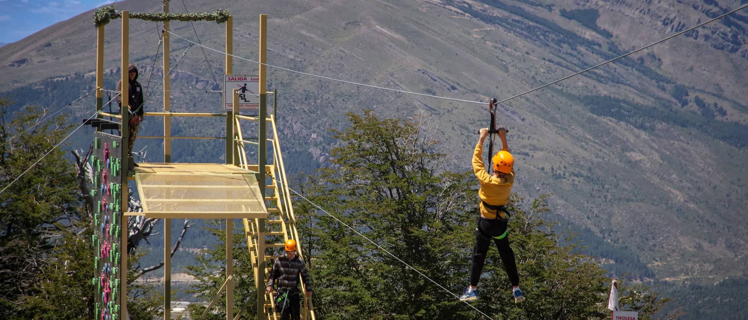 Person seen from behind launching themselves off a zip line with a mountain in the background on a sunny day