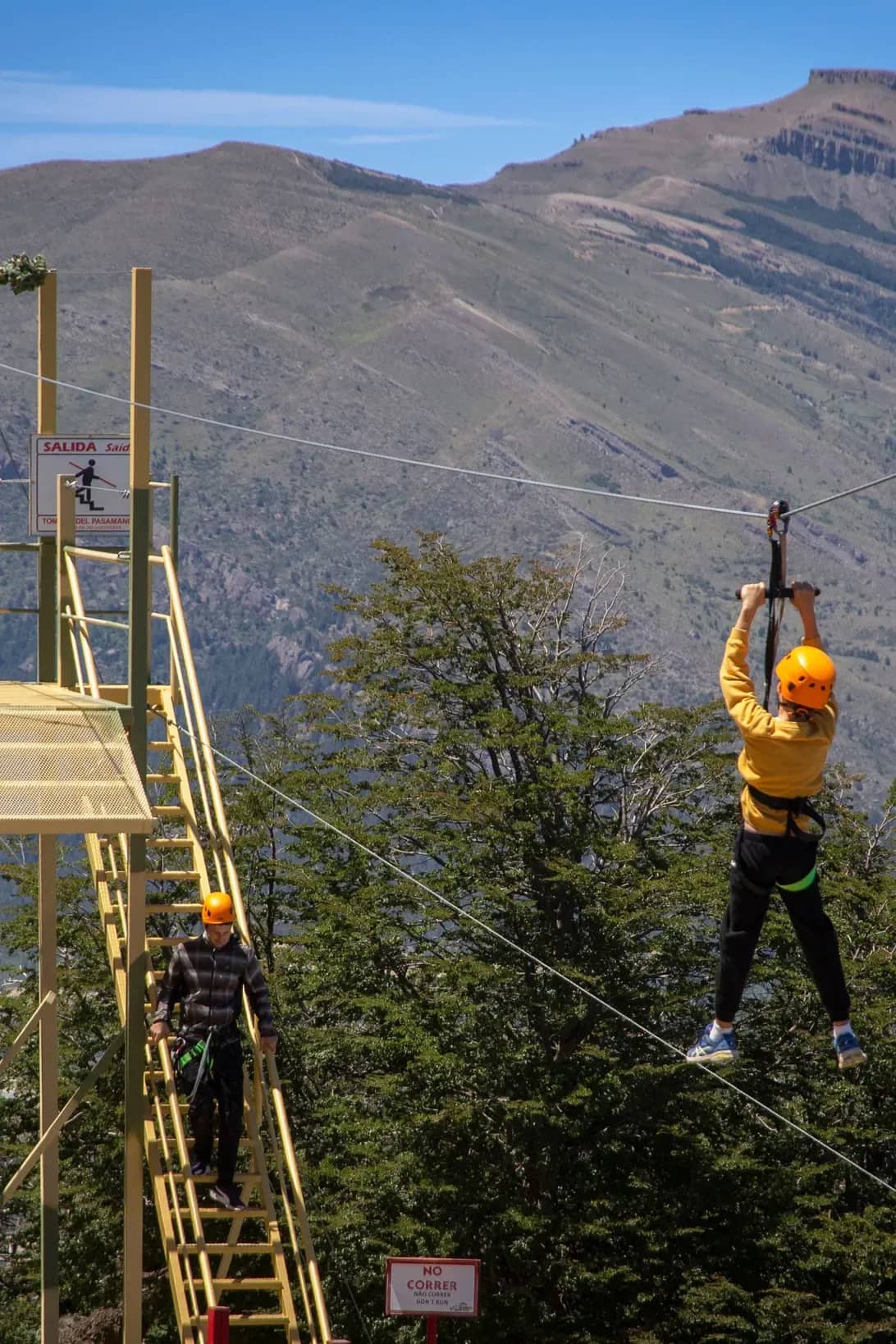 Person seen from behind launching themselves off a zip line with a mountain in the background on a sunny day