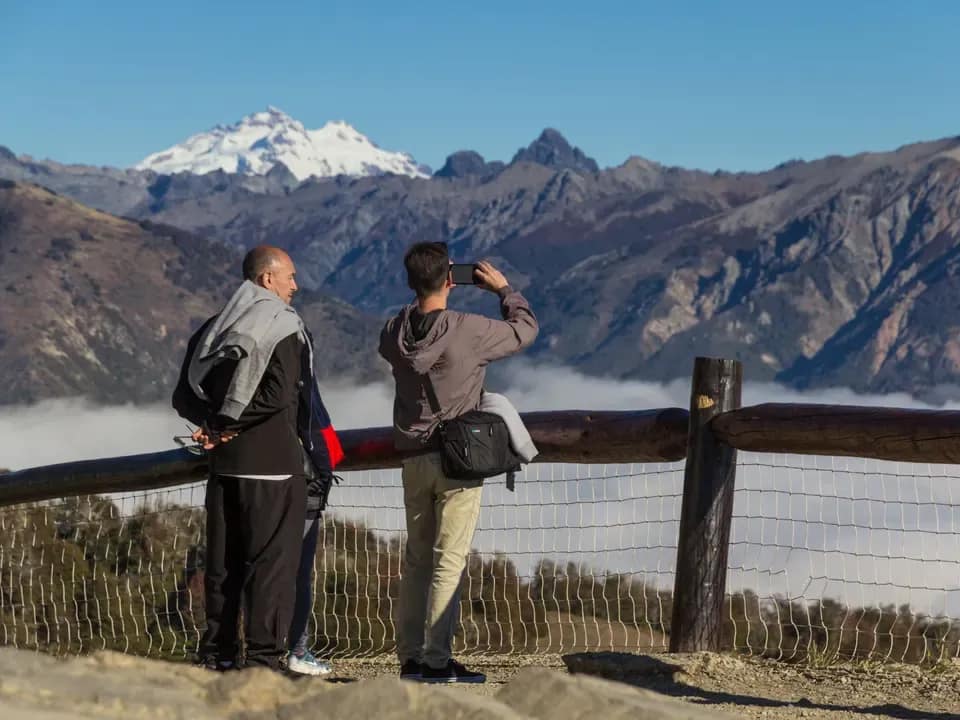 Two people with their backs to the camera admiring the mountains from a balcony of the Teleférico Cerro Otto