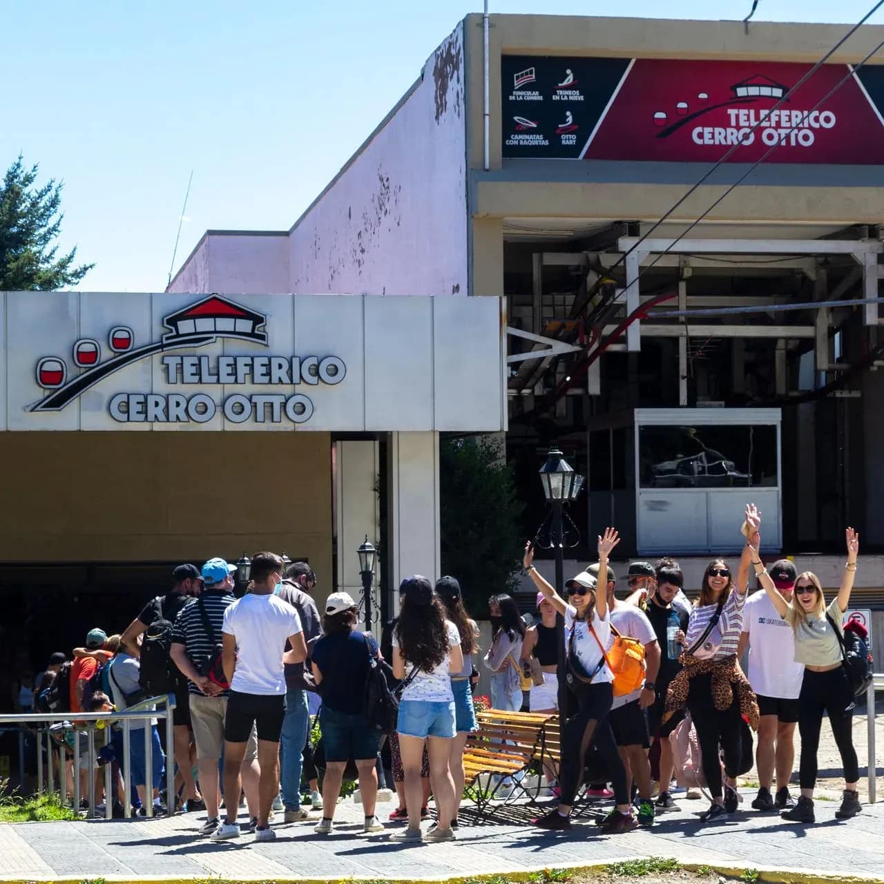Turistas ingresando por la rampa de entrada a la base con un teleférico despegando.