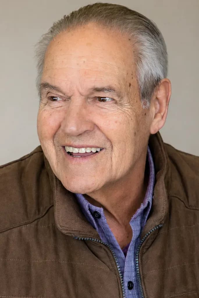 Portrait of the Executive Director of Teleférico Cerro Otto and current President of the Fundación Sara María Furman, wearing a brown vest and a checkered shirt, in an indoor setting with a neutral background.