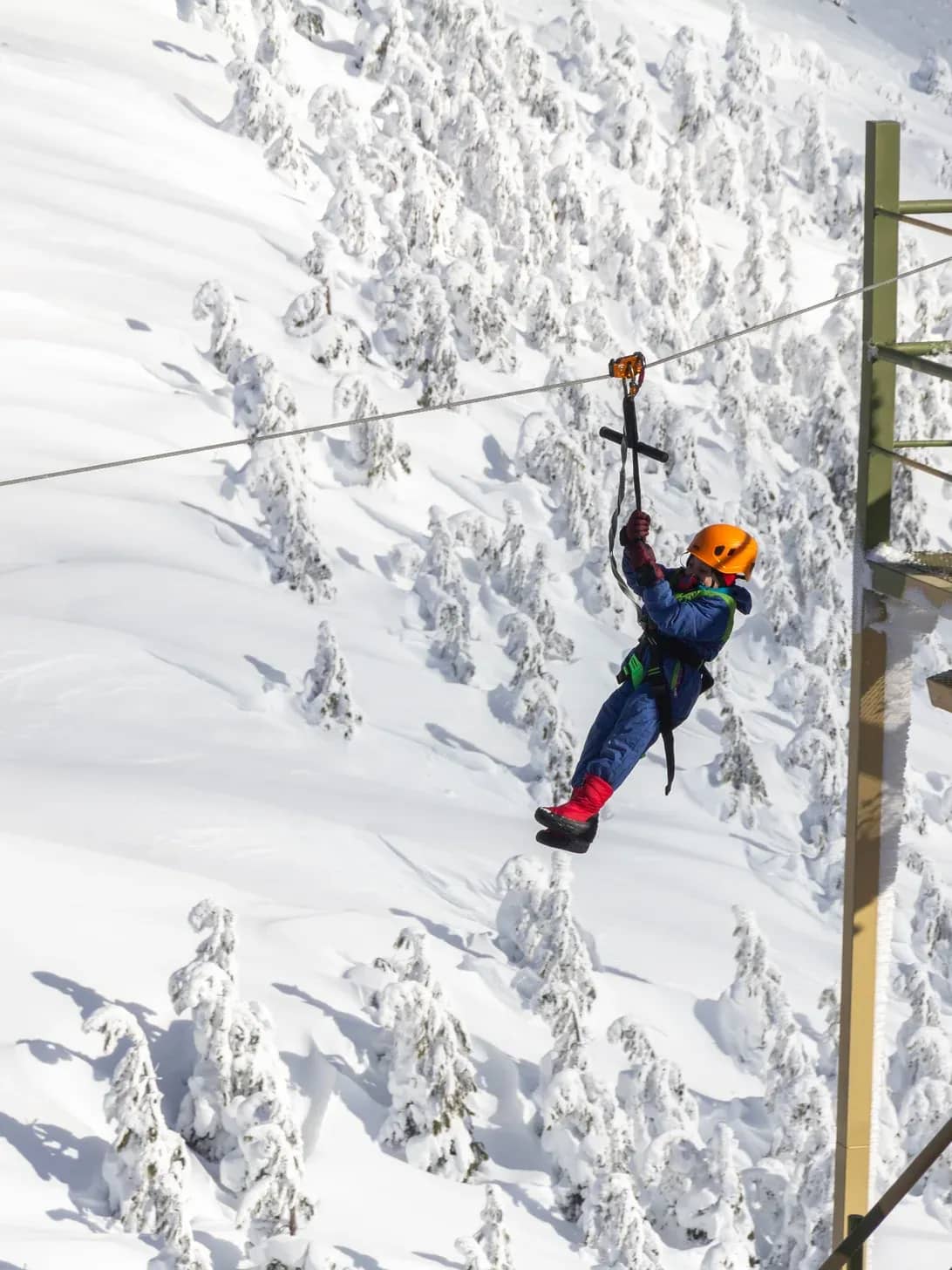 Girl wearing an orange helmet zip-lining with a snowy mountain background