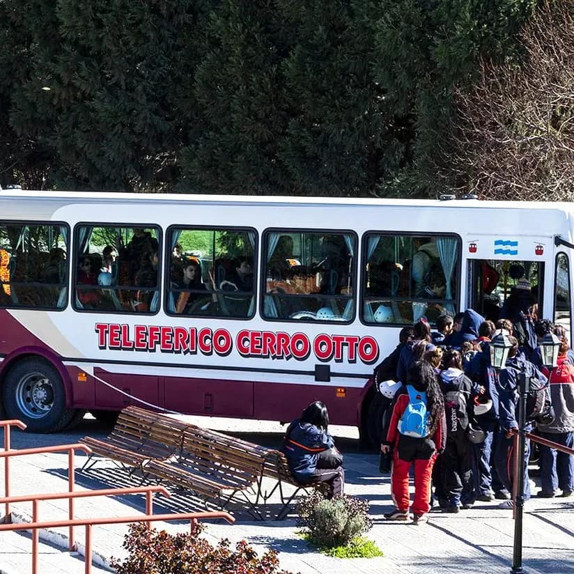 Ônibus turístico gratuito com o logotipo do teleférico Cerro Otto no estacionamento da base, com pessoas desembarcando.
